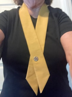 A yellow sash draped around a neck and fastened with a pin at the chest