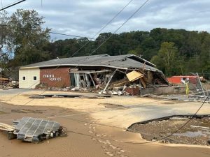 A small brick building after Hurricane Helene. It has crumbled on one side with severe roof and structural damage.