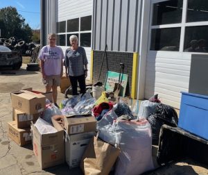 Lynn and Betty, North Carolina Kappas, standing with a large pile of cardboard boxes and bags of donations to sort through.